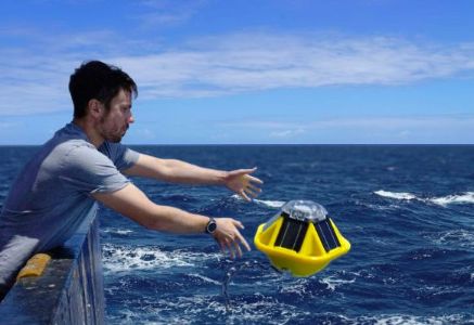 A man throwing a bright yellow Sofar Spotter Buoy into the ocean from a boat